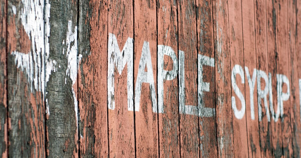 Rustic red wood wall with a faded paint spelling out "maple syrup".